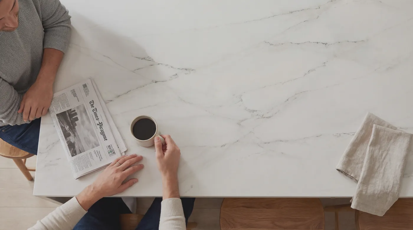 A person reading at a white marble kitchen island with a cup of coffee