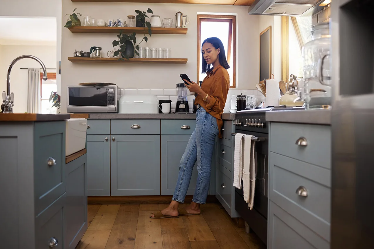 A woman standing in her kitchen looking at her phone